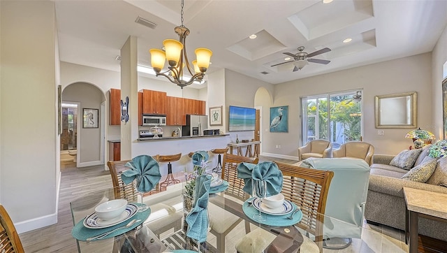 dining space with light hardwood / wood-style flooring, beam ceiling, a high ceiling, coffered ceiling, and ceiling fan with notable chandelier