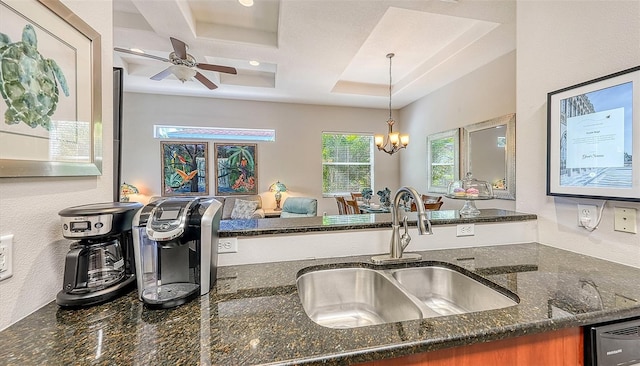 kitchen with sink, hanging light fixtures, dark stone countertops, a raised ceiling, and ceiling fan with notable chandelier