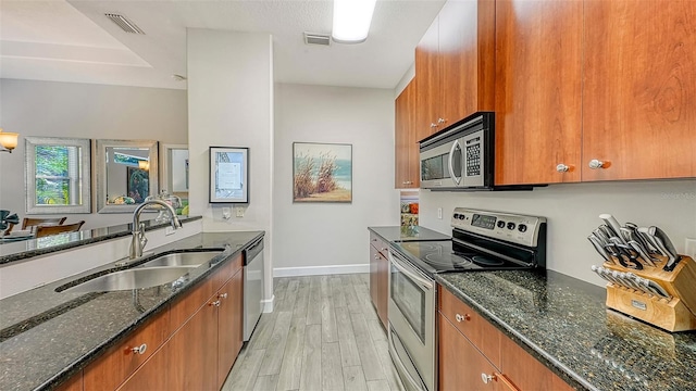 kitchen with appliances with stainless steel finishes, sink, dark stone countertops, and light wood-type flooring