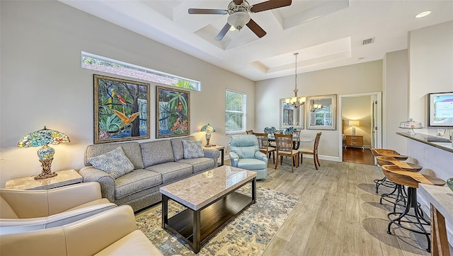 living room with ceiling fan with notable chandelier, coffered ceiling, and light hardwood / wood-style floors