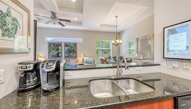 kitchen featuring ceiling fan with notable chandelier, pendant lighting, sink, dark stone counters, and a raised ceiling