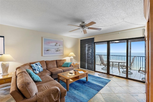 living area with a ceiling fan, a textured ceiling, and a water view