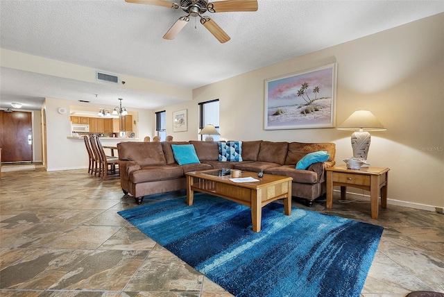 living area featuring stone tile flooring, visible vents, baseboards, and ceiling fan with notable chandelier