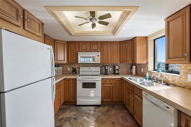 kitchen with brown cabinetry, backsplash, a tray ceiling, and white appliances