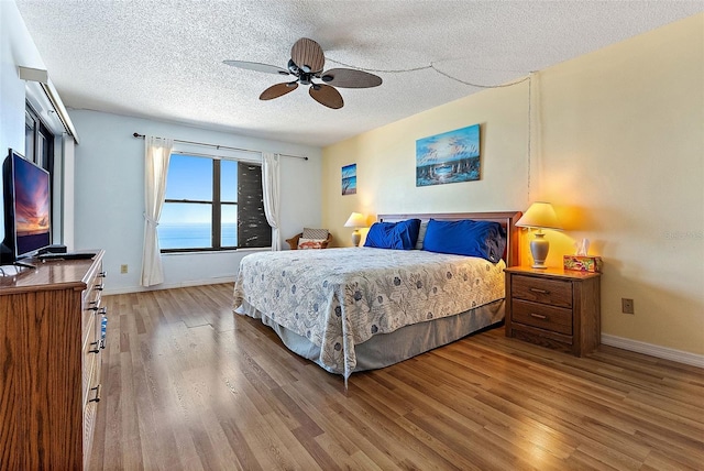 bedroom with baseboards, wood finished floors, a textured ceiling, and ceiling fan