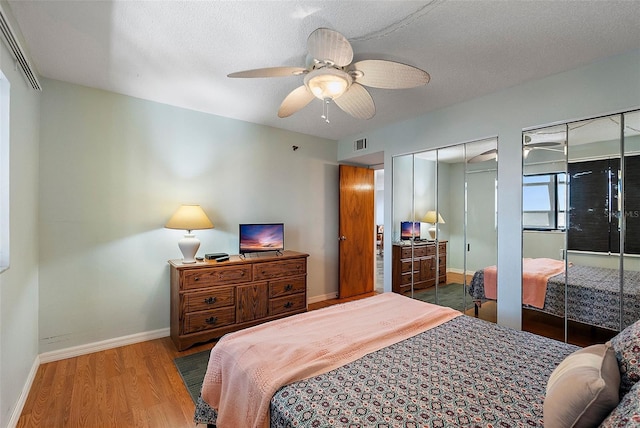bedroom featuring a ceiling fan, wood finished floors, multiple closets, baseboards, and visible vents