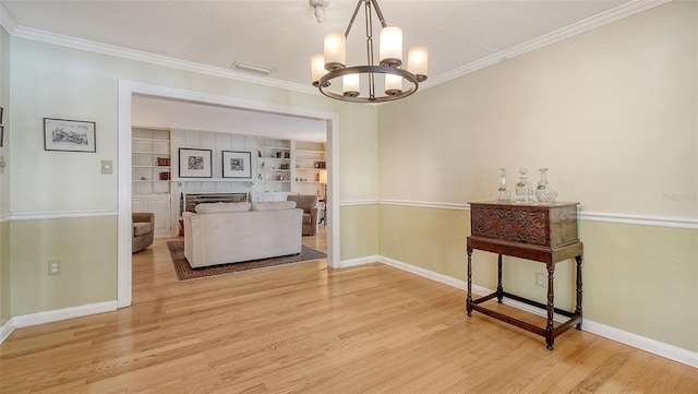 dining area featuring built in features, a fireplace, ornamental molding, a notable chandelier, and light hardwood / wood-style flooring