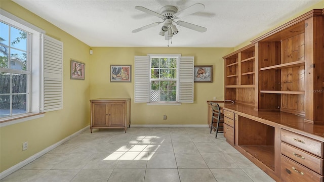 unfurnished office featuring light tile patterned flooring, ceiling fan, built in desk, and a textured ceiling