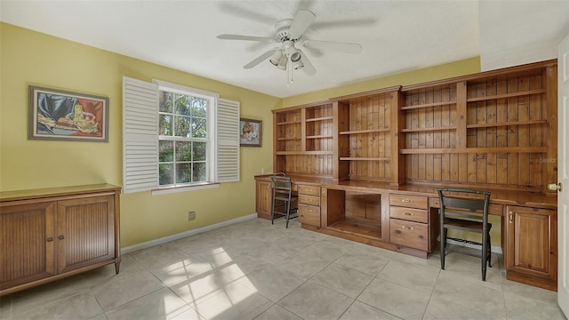 unfurnished office with light tile patterned floors, built in desk, and ceiling fan