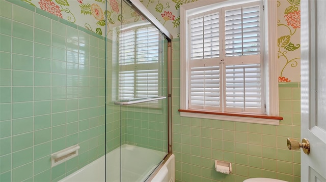 bathroom with a wealth of natural light, shower / bath combination with glass door, and tile walls