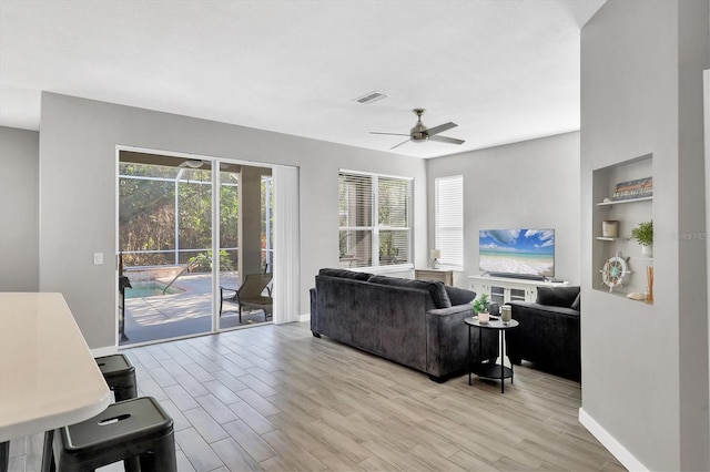 living room featuring built in features, ceiling fan, and light wood-type flooring