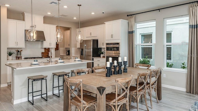 kitchen featuring white cabinetry, appliances with stainless steel finishes, a kitchen island with sink, and decorative light fixtures