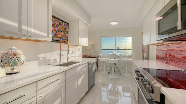 kitchen featuring sink, white cabinets, decorative backsplash, stainless steel appliances, and a water view