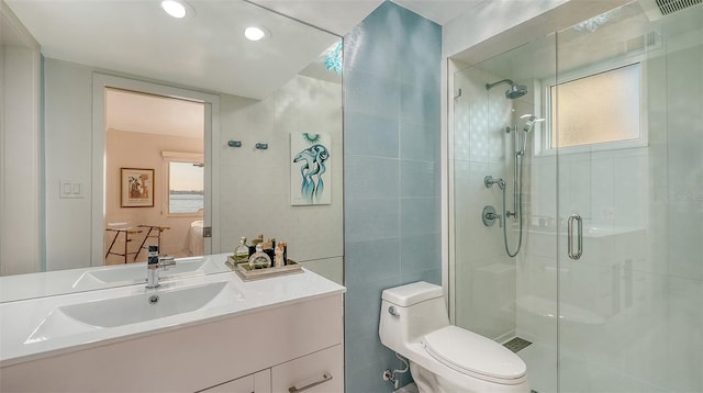 bathroom with vanity, toilet, a shower with door, and tile walls