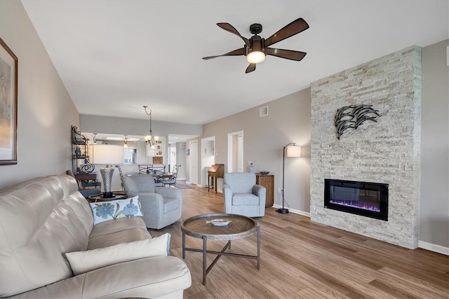 living room with a stone fireplace, ceiling fan with notable chandelier, and light hardwood / wood-style floors