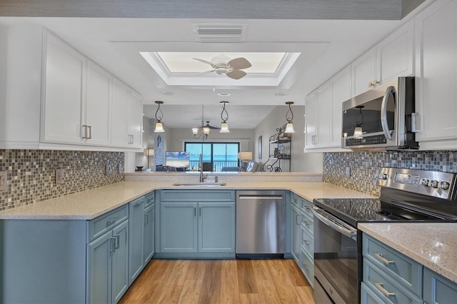 kitchen with a tray ceiling, white cabinets, hanging light fixtures, kitchen peninsula, and stainless steel appliances