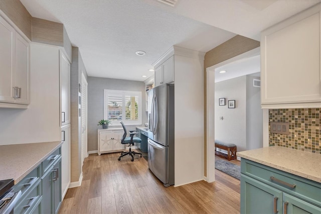 kitchen with stainless steel refrigerator with ice dispenser, tasteful backsplash, built in desk, light hardwood / wood-style flooring, and white cabinets