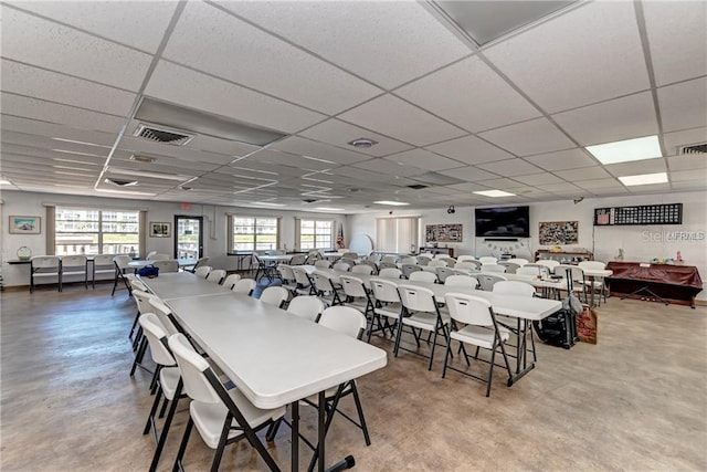 dining space with concrete flooring, a healthy amount of sunlight, and a drop ceiling