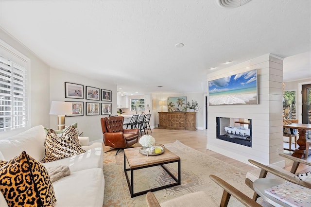 living room with light hardwood / wood-style flooring, a textured ceiling, and a multi sided fireplace