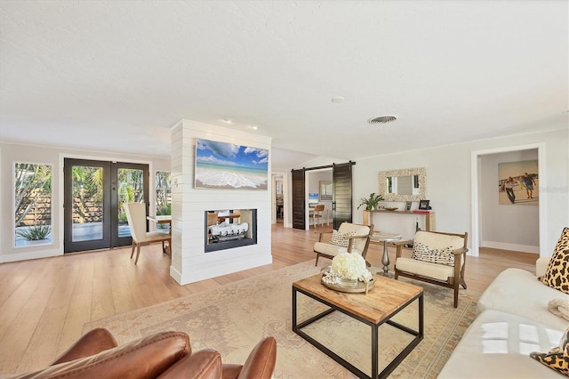 living room with light hardwood / wood-style flooring, a multi sided fireplace, a textured ceiling, a barn door, and french doors