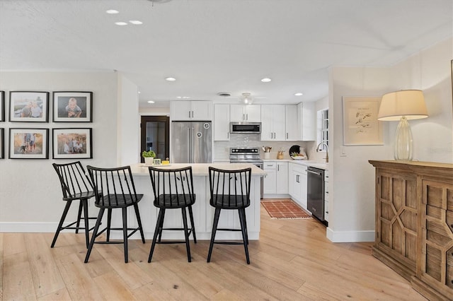 kitchen featuring light hardwood / wood-style flooring, white cabinetry, backsplash, stainless steel appliances, and a kitchen bar