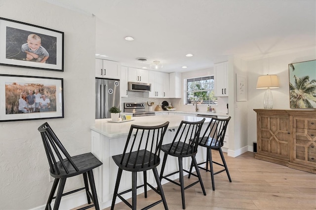 kitchen featuring white cabinetry, stainless steel appliances, a kitchen bar, and light hardwood / wood-style floors