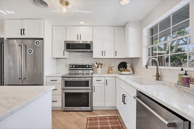 kitchen with appliances with stainless steel finishes, sink, white cabinets, and light wood-type flooring