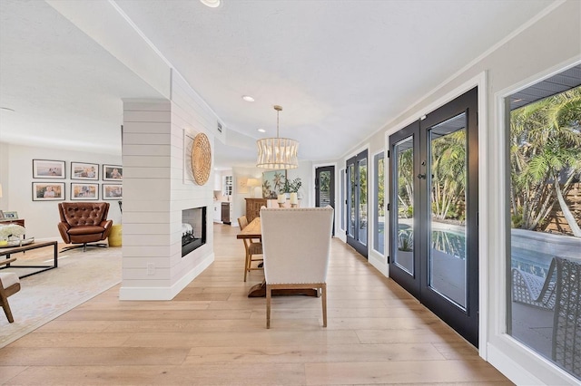 dining room featuring a multi sided fireplace, a chandelier, crown molding, and light hardwood / wood-style flooring