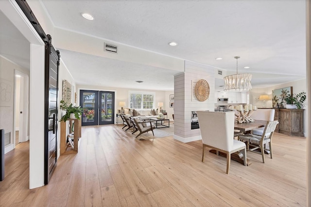 dining space with light hardwood / wood-style flooring, a chandelier, ornamental molding, a barn door, and french doors