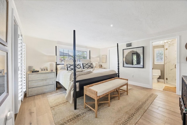 bedroom featuring ensuite bath, a textured ceiling, and light wood-type flooring