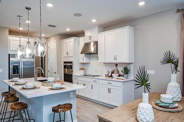 kitchen featuring a breakfast bar, white cabinetry, decorative light fixtures, an island with sink, and stainless steel appliances