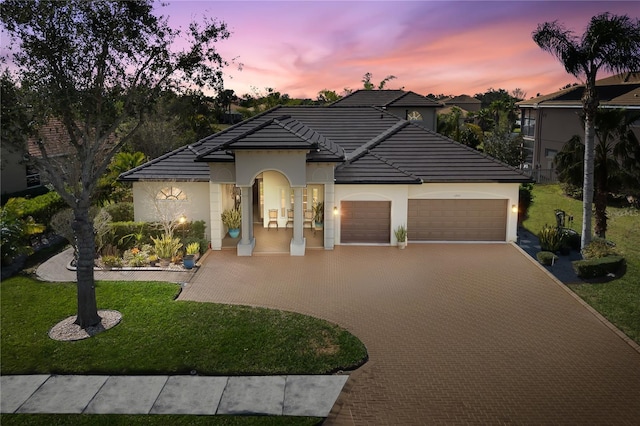 view of front of house with a garage, a tile roof, decorative driveway, a yard, and stucco siding