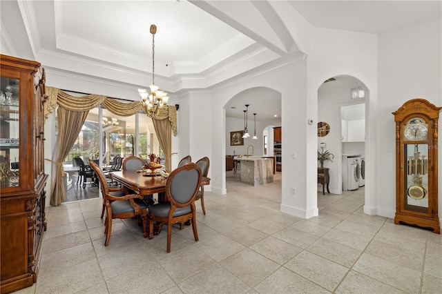 dining area featuring arched walkways, baseboards, a tray ceiling, washing machine and dryer, and a chandelier