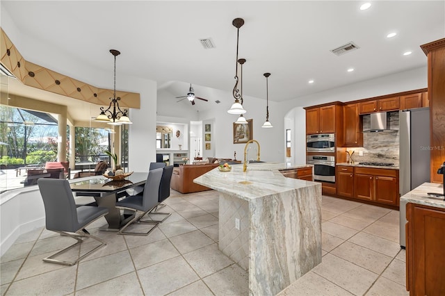 kitchen with pendant lighting, visible vents, open floor plan, wall chimney range hood, and light stone countertops