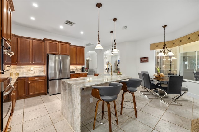 kitchen with arched walkways, pendant lighting, stainless steel appliances, a spacious island, and visible vents