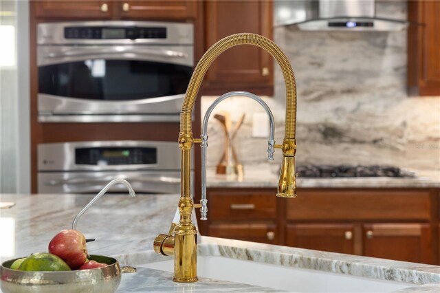 details featuring double oven, brown cabinets, a sink, and exhaust hood