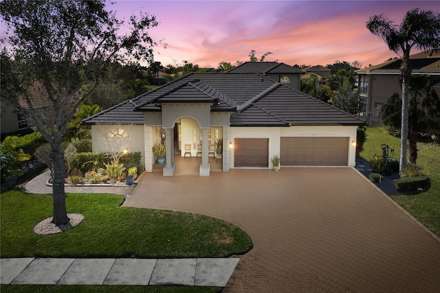 view of front of house with an attached garage, a yard, stucco siding, a tile roof, and decorative driveway