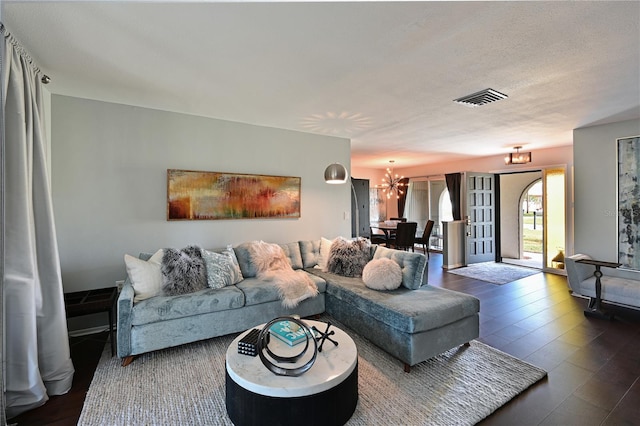 living room featuring an inviting chandelier, dark wood-type flooring, and a textured ceiling