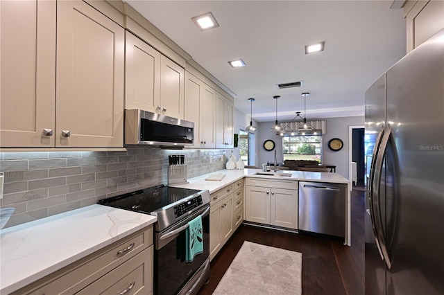 kitchen featuring sink, stainless steel appliances, light stone countertops, decorative light fixtures, and kitchen peninsula