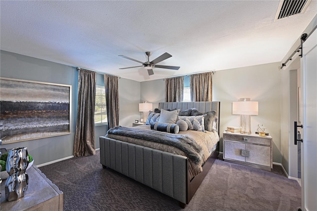 bedroom featuring ceiling fan, a barn door, a textured ceiling, and dark colored carpet