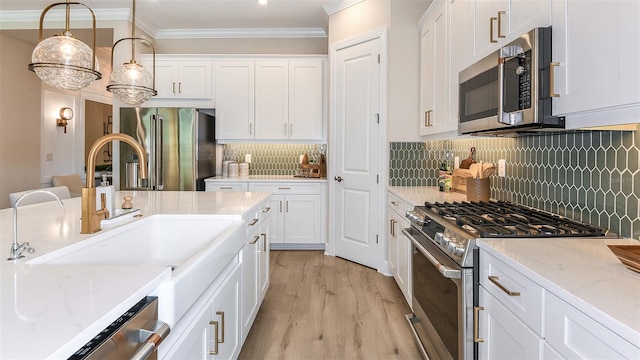 kitchen with hanging light fixtures, premium appliances, ornamental molding, light stone countertops, and white cabinets