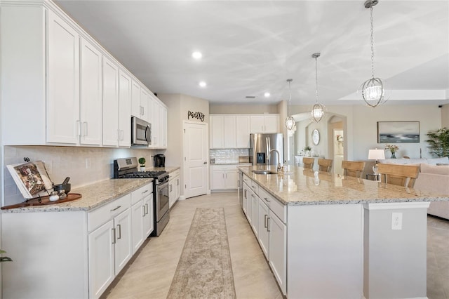 kitchen featuring pendant lighting, white cabinets, stainless steel appliances, and a large island with sink