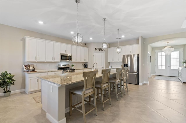 kitchen with appliances with stainless steel finishes, hanging light fixtures, a kitchen breakfast bar, an island with sink, and white cabinets