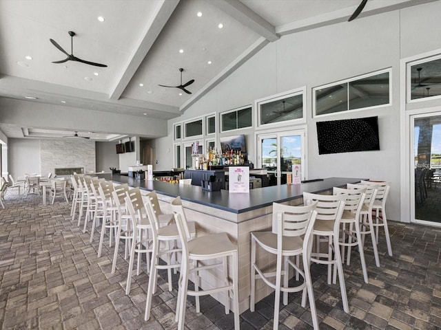 kitchen with ceiling fan, a kitchen bar, beam ceiling, and high vaulted ceiling