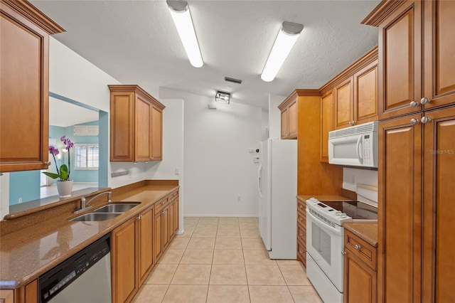 kitchen with light tile patterned flooring, a sink, brown cabinets, and white appliances