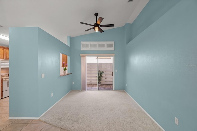 empty room featuring light colored carpet, vaulted ceiling, light tile patterned floors, baseboards, and a ceiling fan
