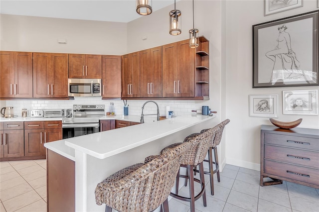 kitchen featuring light tile patterned flooring, a kitchen bar, decorative light fixtures, kitchen peninsula, and stainless steel appliances