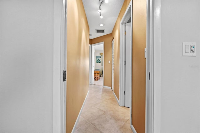 hall with light tile patterned flooring, track lighting, and a textured ceiling