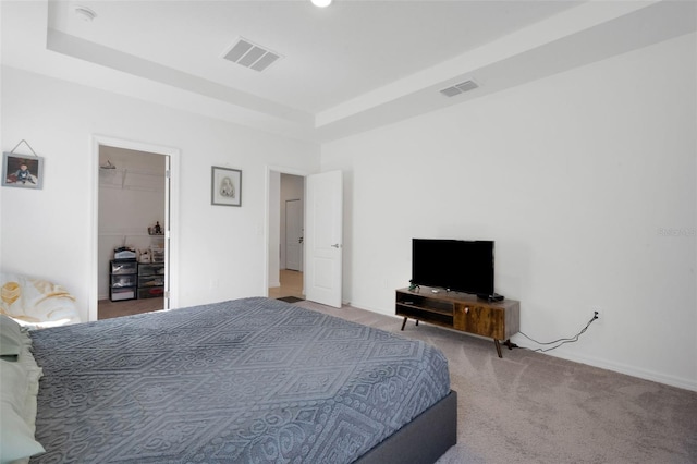 bedroom featuring carpet flooring, a tray ceiling, and a walk in closet