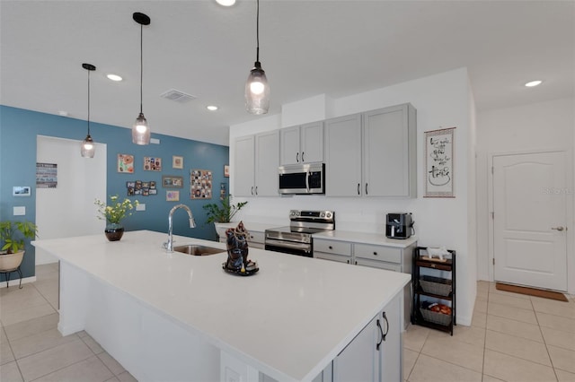 kitchen with an island with sink, stainless steel appliances, sink, and hanging light fixtures